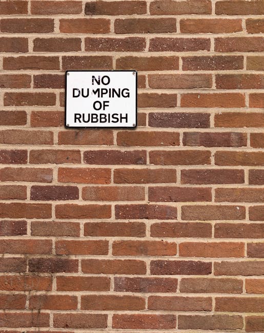 A row of three large wheelie bins positioned on the pavement in front of a building with a graffiti-covered brick wall. The first bin is grey with a closed lid, while the second and third bins are bla